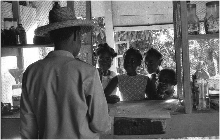 Milieu rural, scène de vie quotidienne. Enfants cherchant des confiseries et des hommes buvant un punch à l'épicerie-bar ; trois enfants réalisant des travaux ménagers