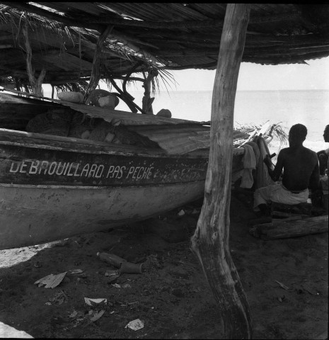 Le Carbet. Bar-café avec des enseignes publicitaires ; pêcheurs arrangeant leurs filets et leurs canots