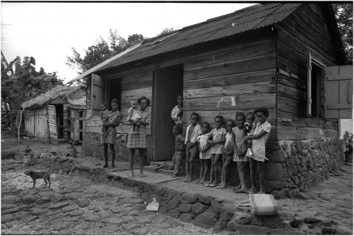 Trinité. scène de vie quotidienne : logement au milieu rural (case traditionnelle en bois), enfants et parents ; vue sur le littoral : baie